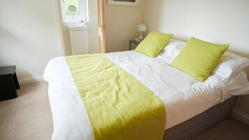 A neatly made bed with a white and yellow bedspread, two green pillows, and a bedside table with a lamp.