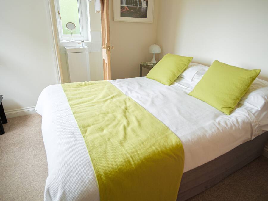 A neatly made bed with a white and yellow bedspread, two green pillows, and a bedside table with a lamp.