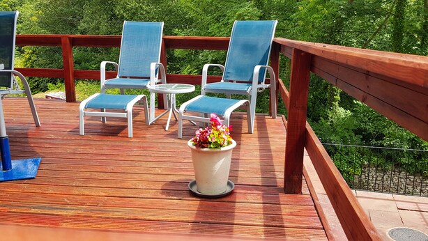 A wooden deck with outdoor furniture, including chairs and a table, and a potted plant with flowers. - Mill Lodge Brecon Beacons (Abergavenny)