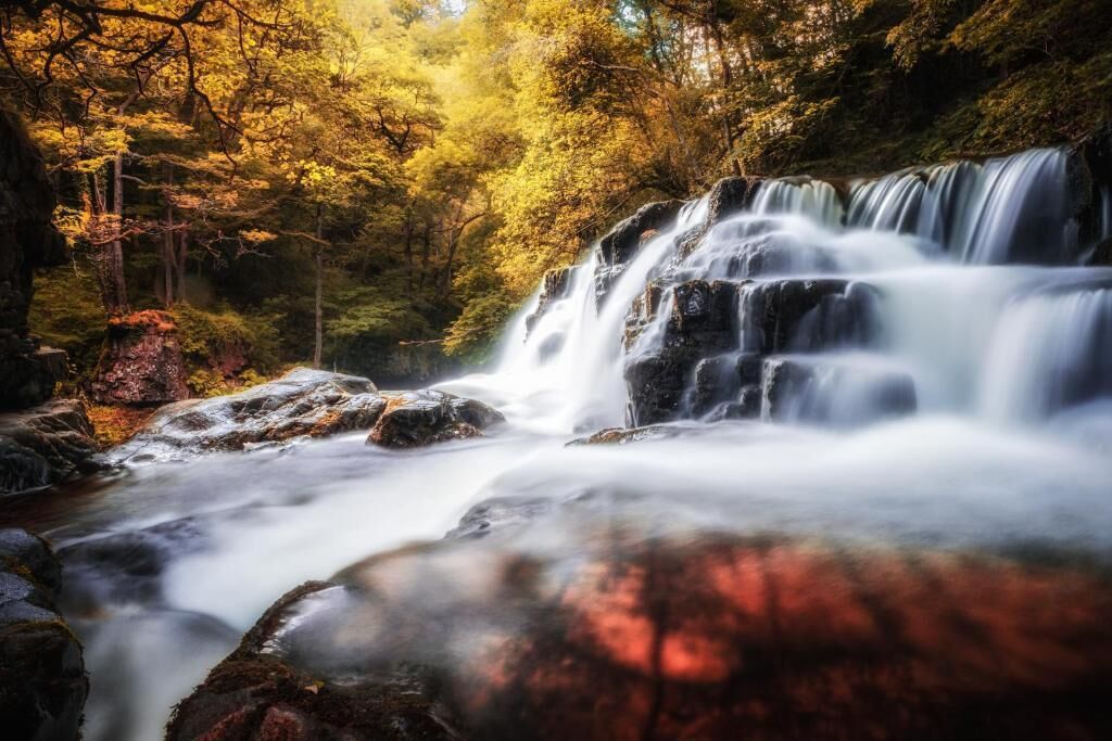 Una cascada en un área boscosa con rocas y árboles.