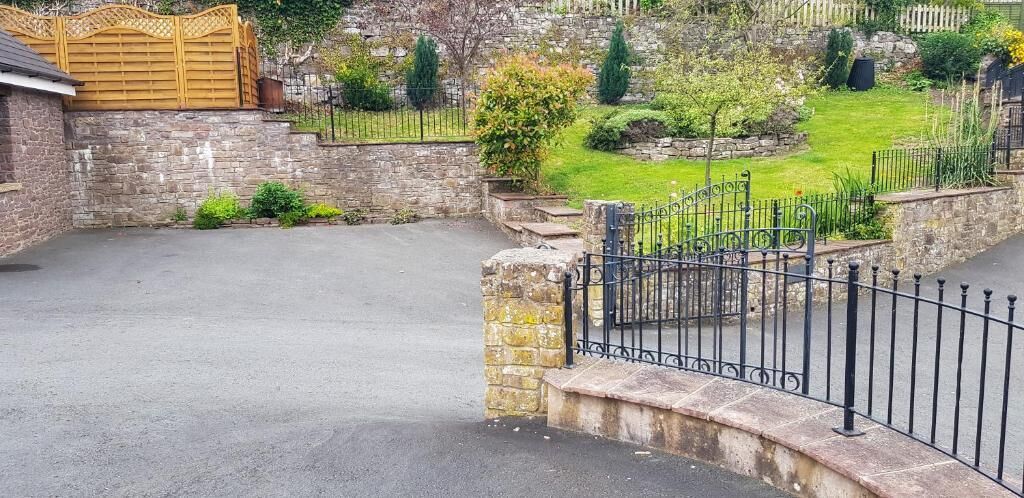 A paved driveway leading to a gated entrance with a stone wall and a metal fence.