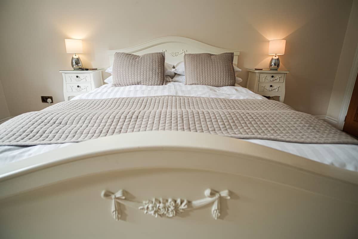 A neatly made bed with a quilted cover, two bedside lamps, and a decorative headboard.
