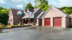 A two-story house with a garage, a front porch with potted plants, and a driveway. - Mill Lodge Brecon Beacons (Abergavenny)
