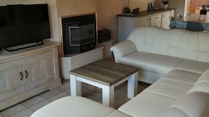 A living room with a white sofa, a television, a fireplace, and a small table. - Vacation home for 10 pers in Westende: Rest on the Coast (Middelkerke)