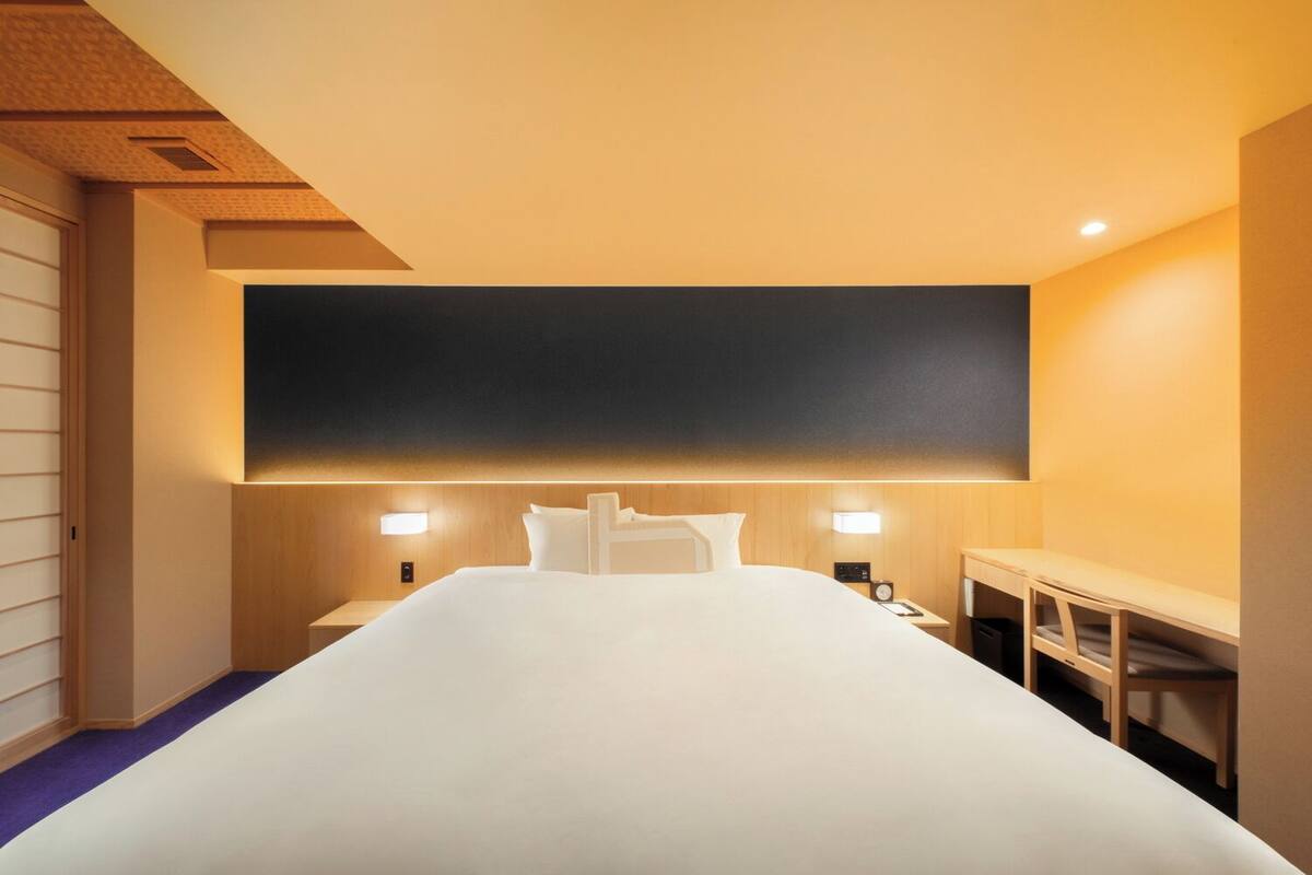 Une chambre d’hôtel dotée d’un grand lit, de tables de chevet, d’une petite table et d’une tête de lit avec éclairage intégré.
