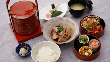 Un repas japonais traditionnel composé de riz, de poisson et de divers accompagnements, servi sur une table avec un récipient rouge et un bol noir de soupe.