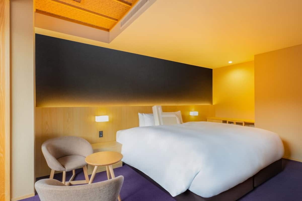 Une chambre d’hôtel avec un grand lit, deux chaises, une petite table et une tête de lit en bois.