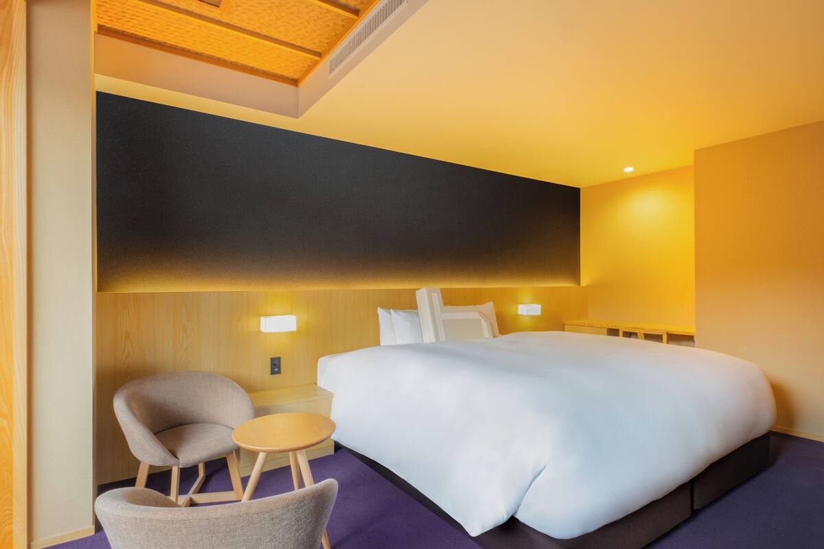 Une chambre d’hôtel avec un grand lit, une petite table ronde, deux fauteuils et une tête de lit en bois.
