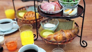 Un plateau de petit-déjeuner comprenant des œufs, de la viande et des légumes, accompagné de tasses de café et de jus d’orange.