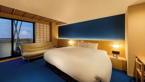 Une chambre d’hôtel avec un grand lit, un canapé, une table de chevet avec une horloge et une vue sur l’extérieur grâce à une grande fenêtre.