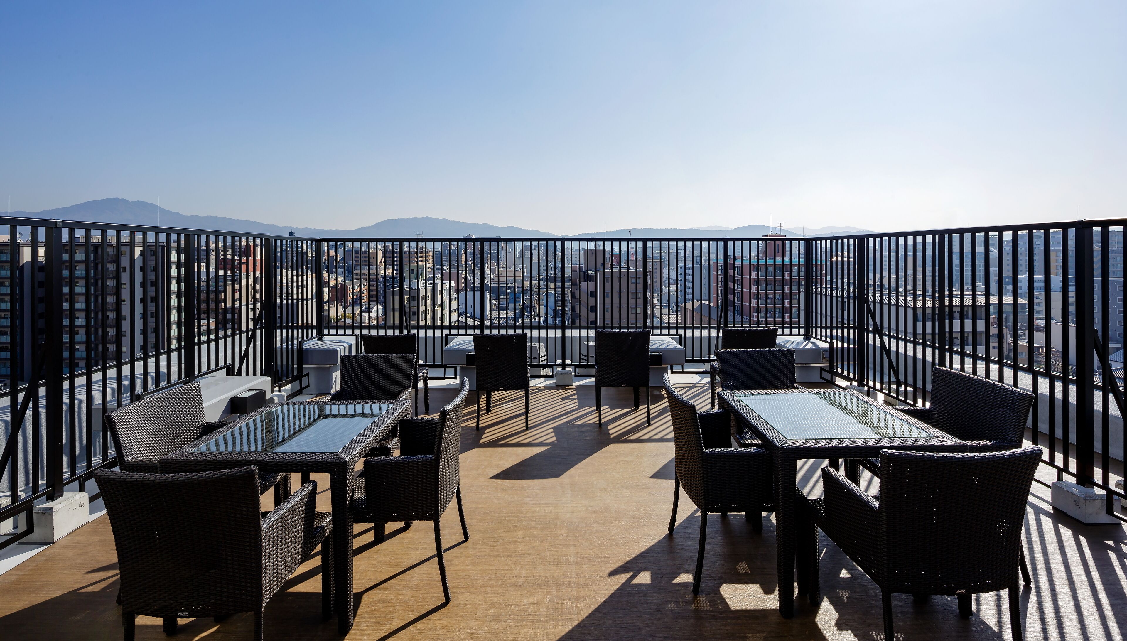 Une terrasse sur le toit, dotée de rampes en métal noir, de meubles en osier et offrant une vue sur la ville.