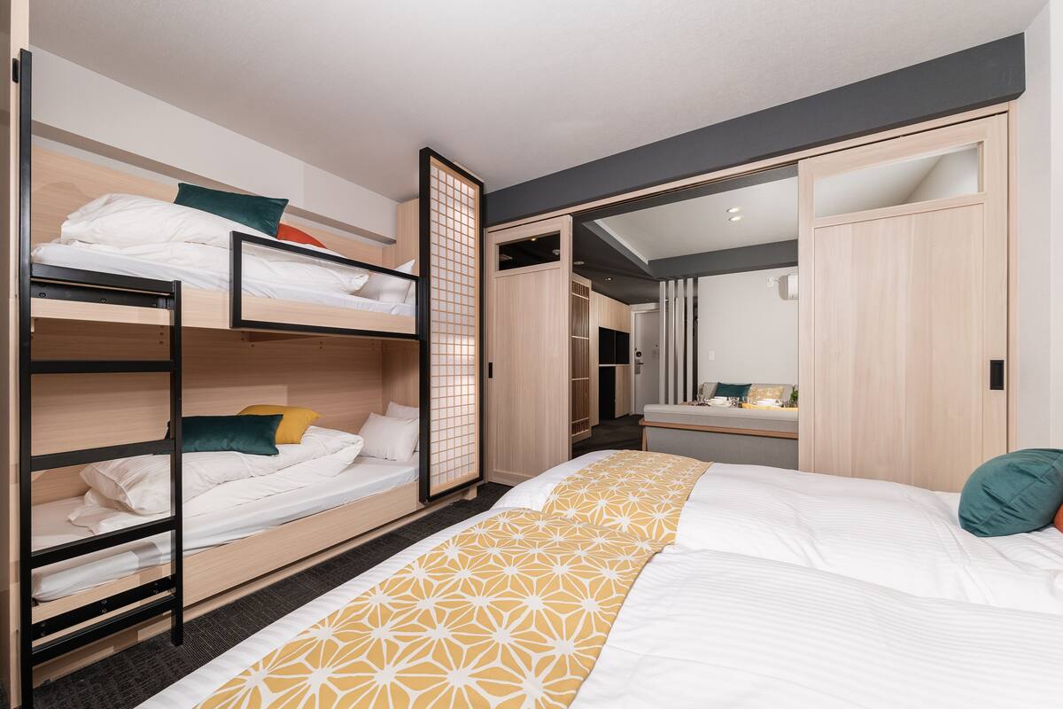 Une chambre d’hôtel moderne avec des lits superposés, un grand lit, un dressing et une salle de bain avec un miroir.