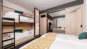 Une chambre d’hôtel moderne avec des lits superposés, un grand lit, un dressing et une salle de bain avec un miroir.