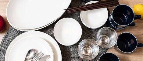 A table set with plates, bowls, chopsticks, and glasses, with apples and a lemon on the table.