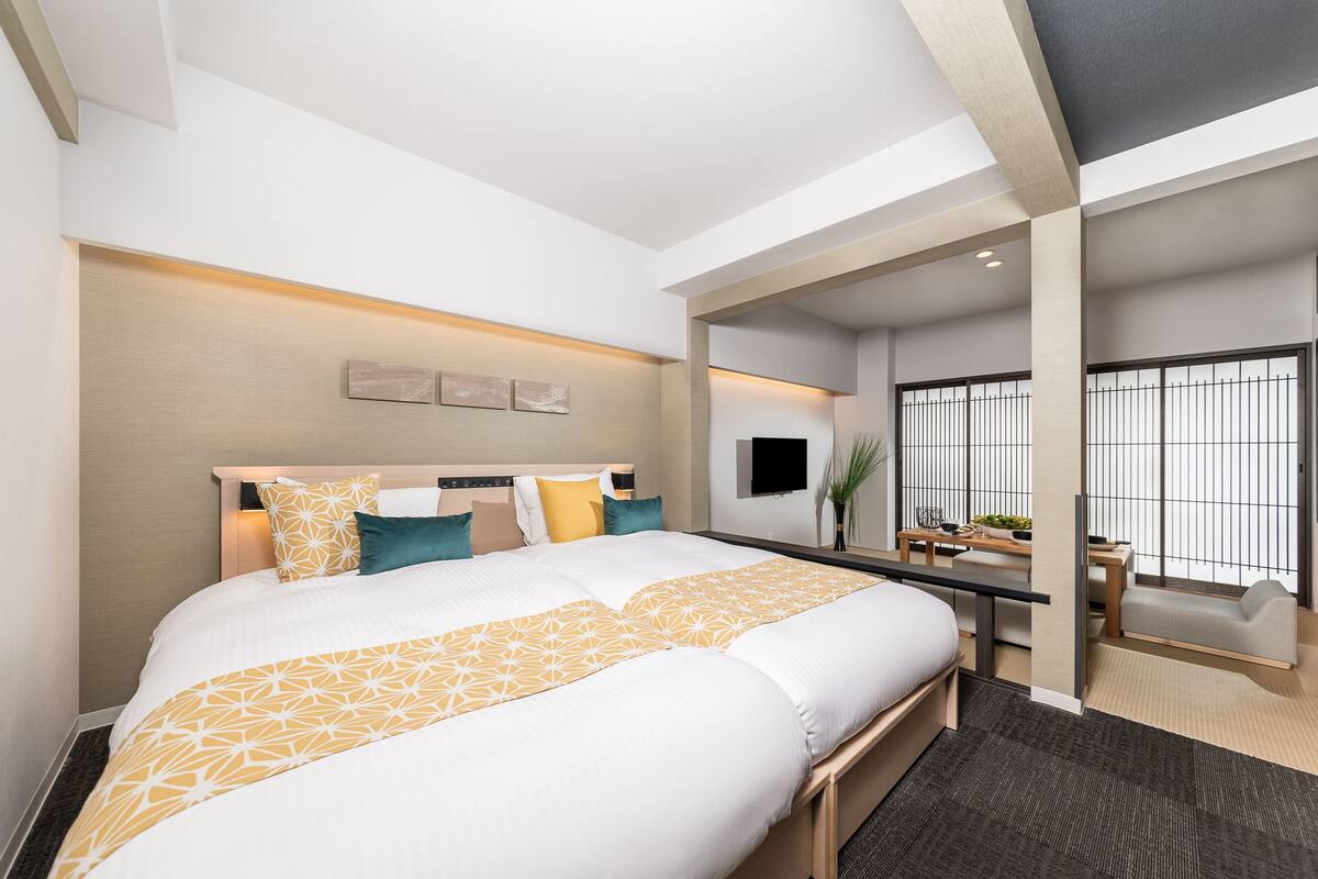 Une chambre d’hôtel moderne, dotée d’un grand lit, d’un bureau et offrant une vue sur la ville grâce à de grandes fenêtres.