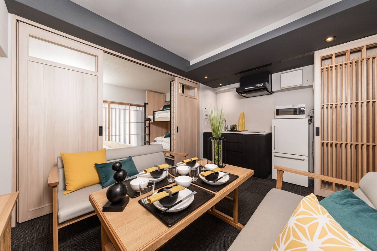 Une chambre d’hôtel compacte comprenant un coin repas, une kitchenette et un canapé avec des coussins.