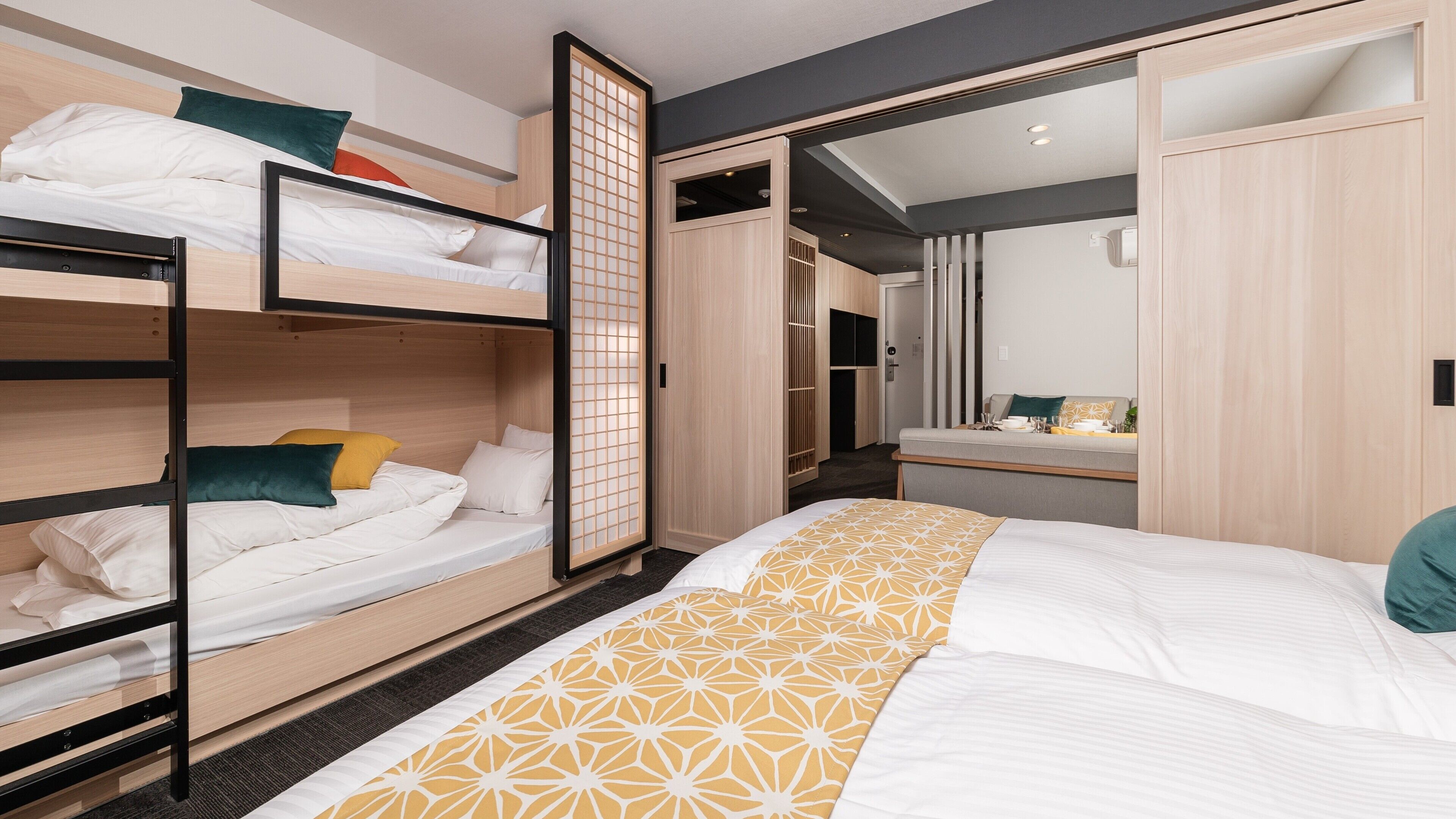 A room with bunk beds, a large bed with a patterned bedspread, a wardrobe, and a mirror.
