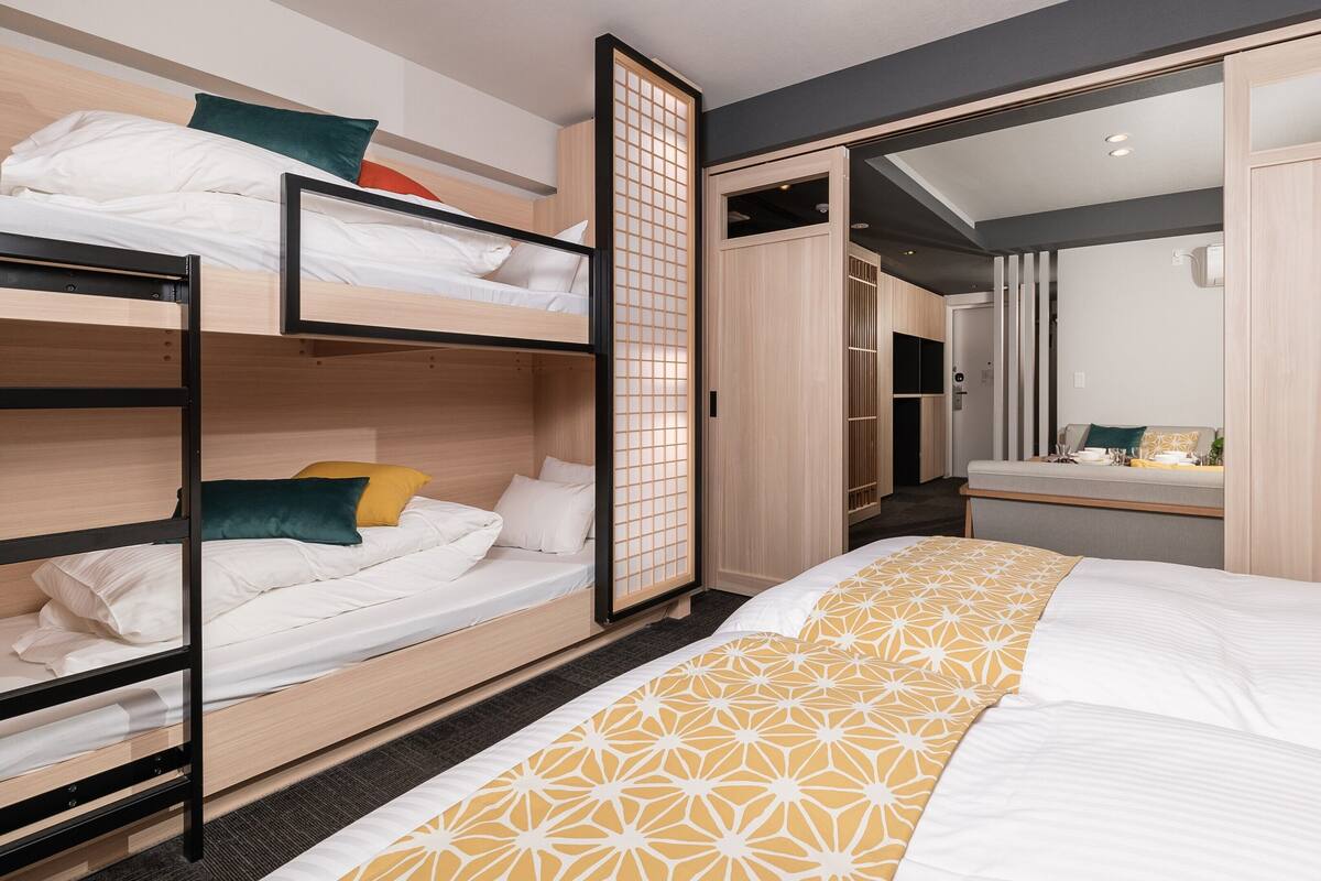 Une chambre avec des lits superposés, un grand lit recouvert d’une couvre-lit à motifs, une armoire et un miroir.