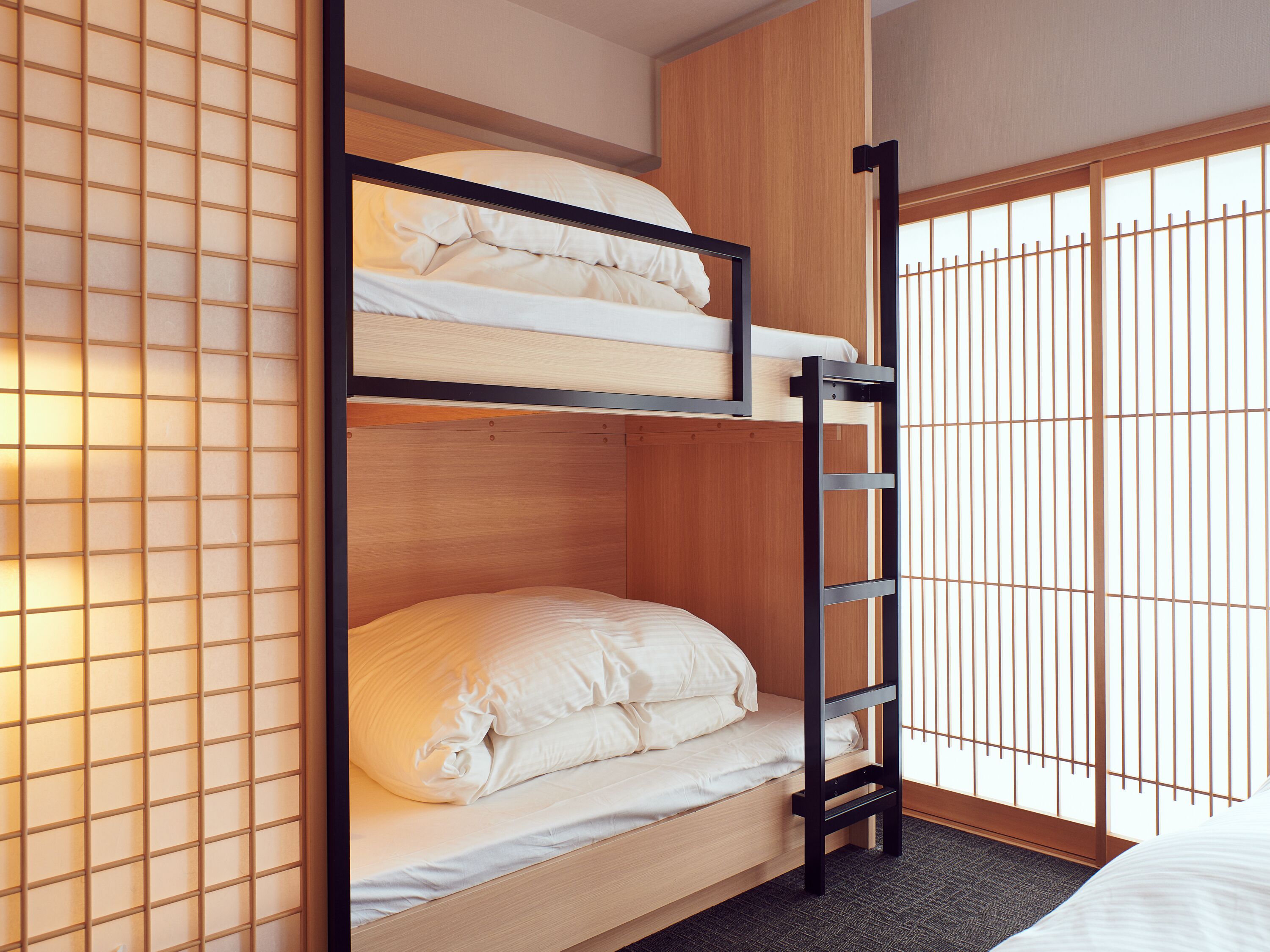 Una cama litera con escalera, paneles de madera y vistas a una ventana con persianas verticales.