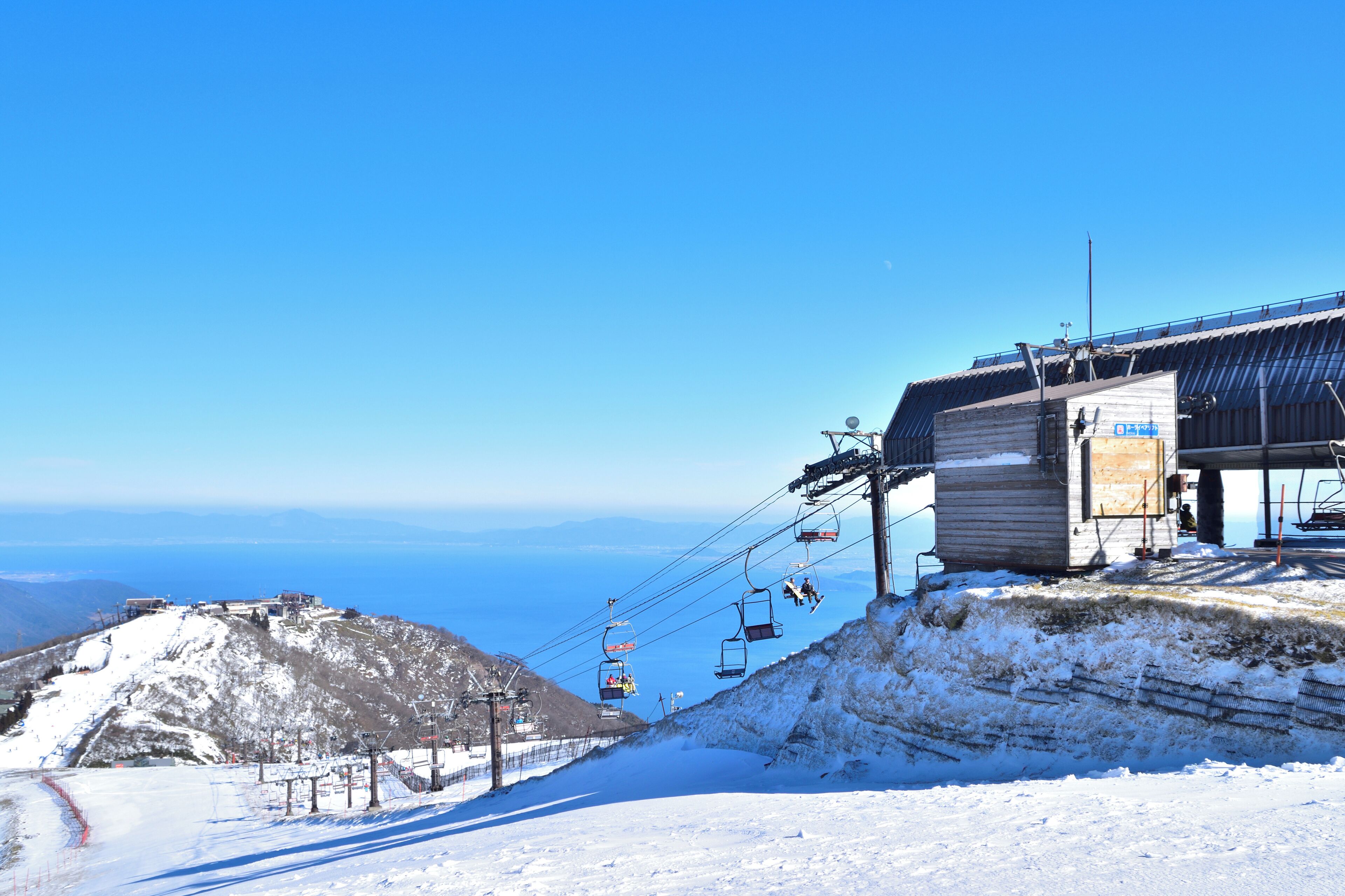 Une piste de ski enneigée, avec un télésiège et un bâtiment portant une enseigne.