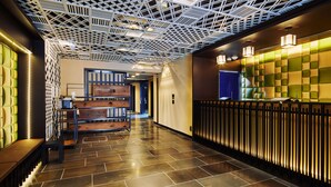 Eine moderne Hotelhalle mit einem geometrischen Deckenmuster, einem Empfangsbereich in Grün- und Gelbtönen und einem polierten Steinboden.