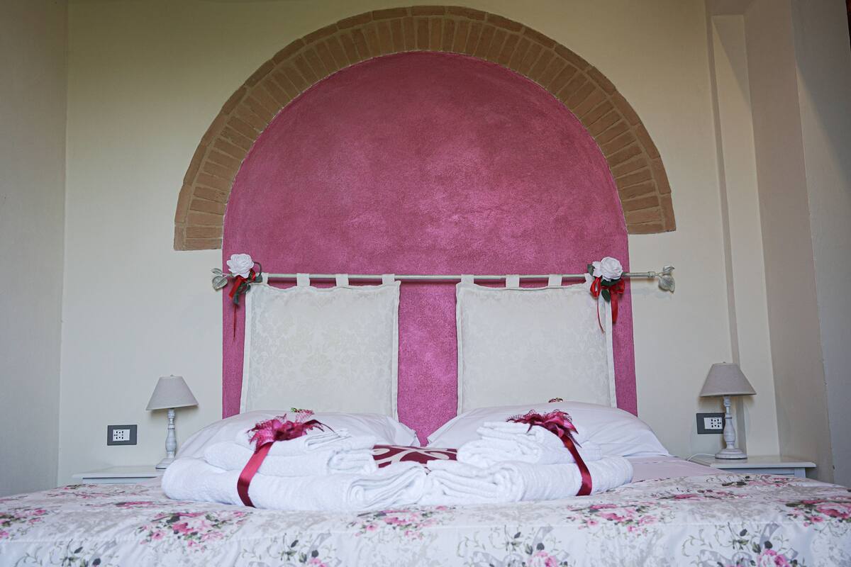 A neatly made bed with floral bedding, a pink headboard, and a brick arch above it.
