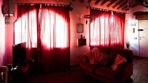 A cozy living room with a red sofa, a television, and a kitchen area with a refrigerator and stove. - Le Undici Lune (San Gimignano)