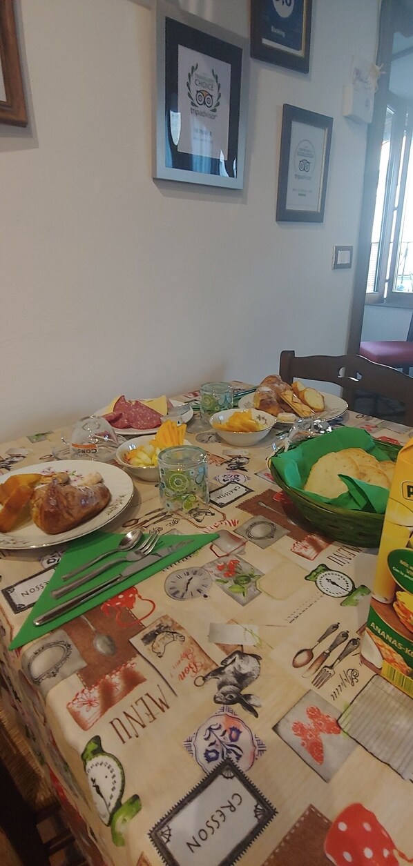 A dining table with various food items and utensils, set against a wall with framed certificates.