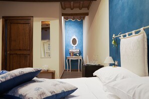 A hotel room with a bed, pillows, a nightstand with a lamp, a small table with a mirror, and a blue accent wall.