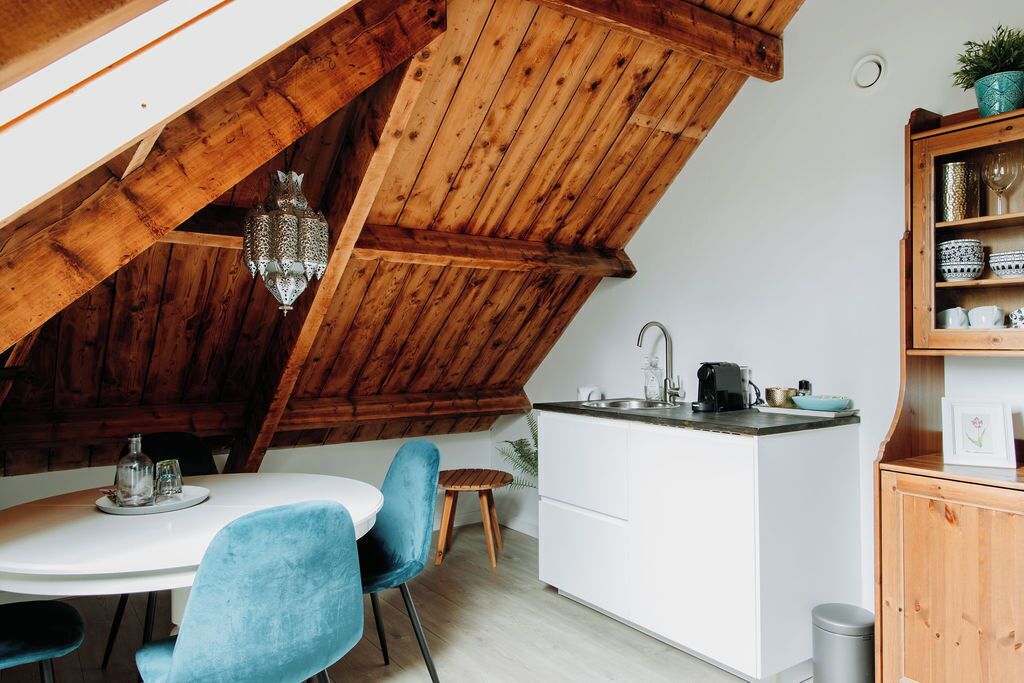 A kitchen with a wooden ceiling, white cabinets, a small island with a sink, and blue chairs.