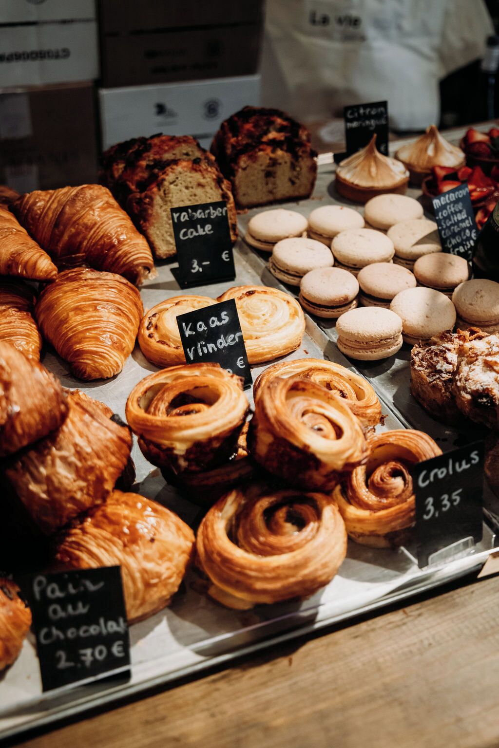 Eine Auswahl an Backwaren in einer Bäckerei, darunter Croissants, Macarons und andere Gebäckstücke, mit Preisanhängern.