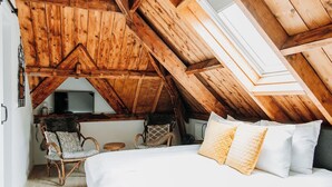 A cozy attic bedroom with a sloped ceiling, a bed with white linens, two wicker chairs, and a small table. - Bergen1928 (Bergen)