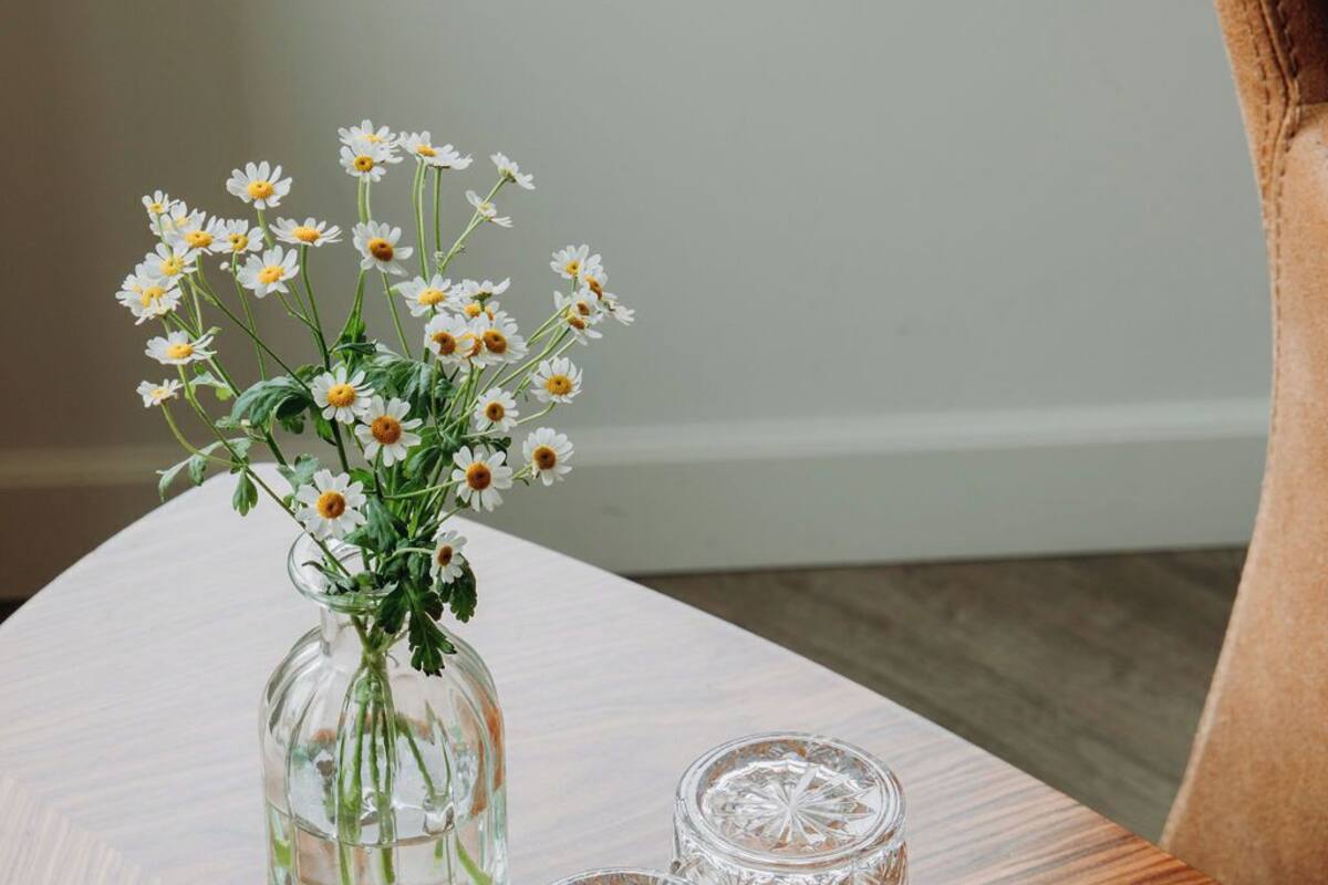 A wooden table with a glass vase containing white flowers and three glass decanters.