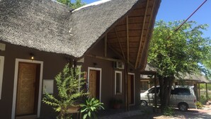 A building with a thatched roof and a wooden door with a geometric design. - Laphroiag Luxury Chalets (Maun)