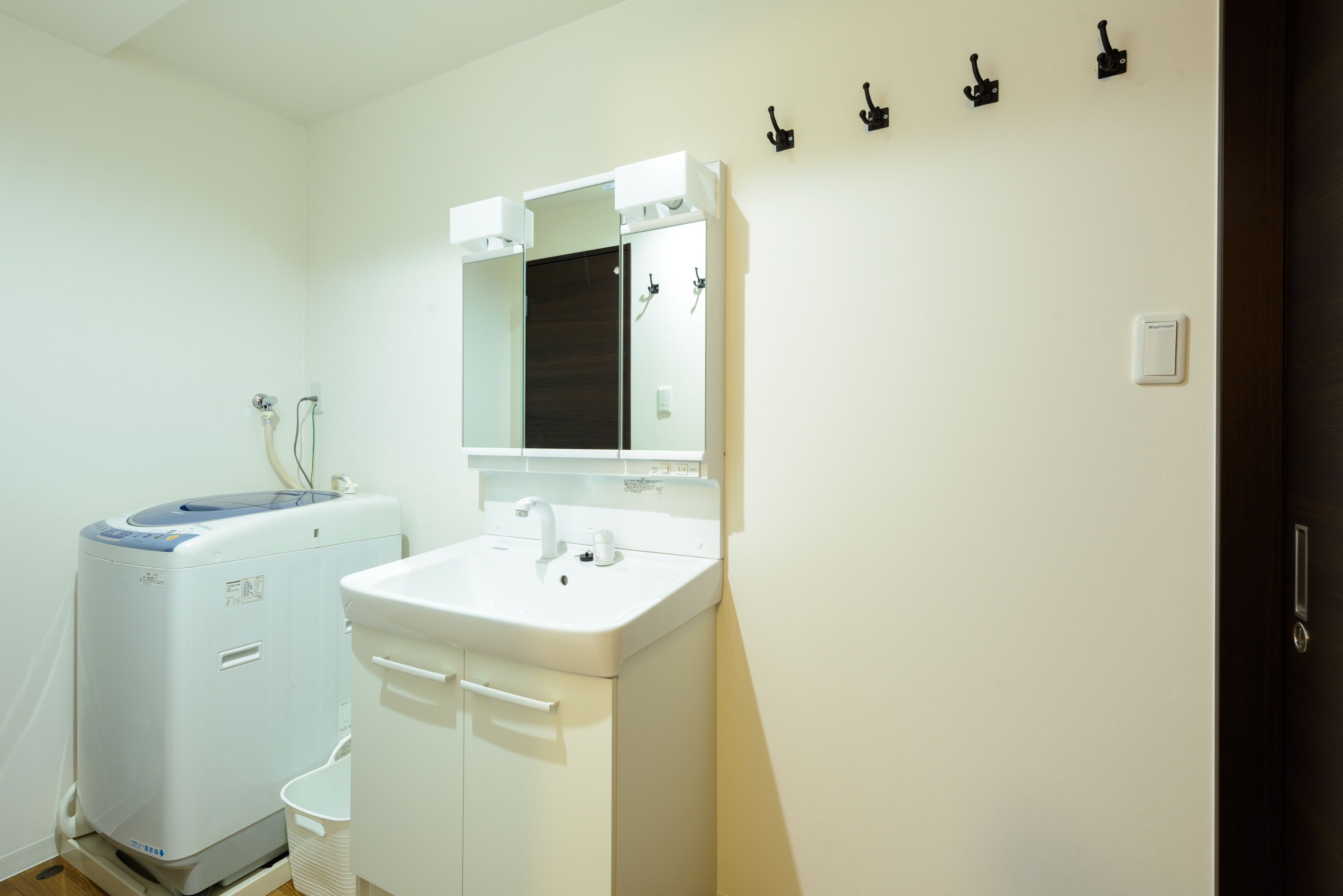 A small, clean bathroom with a white sink, mirror, and a compact washing machine.