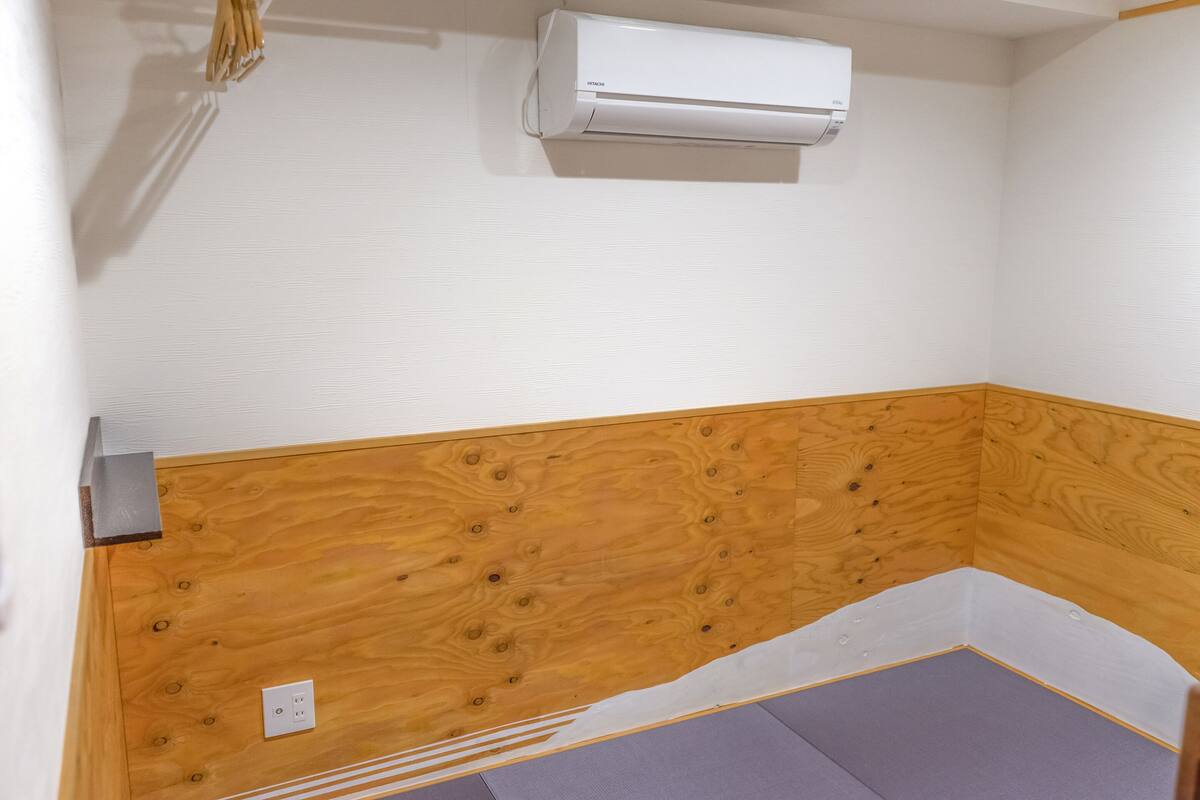 Ein Zimmer mit einer Holzwand, einer weißen Klimaanlage und einer violetten Matte auf dem Boden.
