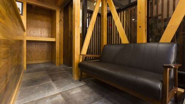 A wooden interior with a black leather sofa, wooden beams, and a tiled floor. - Guest House Koenji Junjo Hotel (Tokyo)