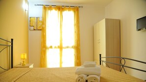 A hotel room with a bed, a bedside lamp, a wardrobe, and a window with curtains. - B&B Erminia (Presicce-Acquarica)