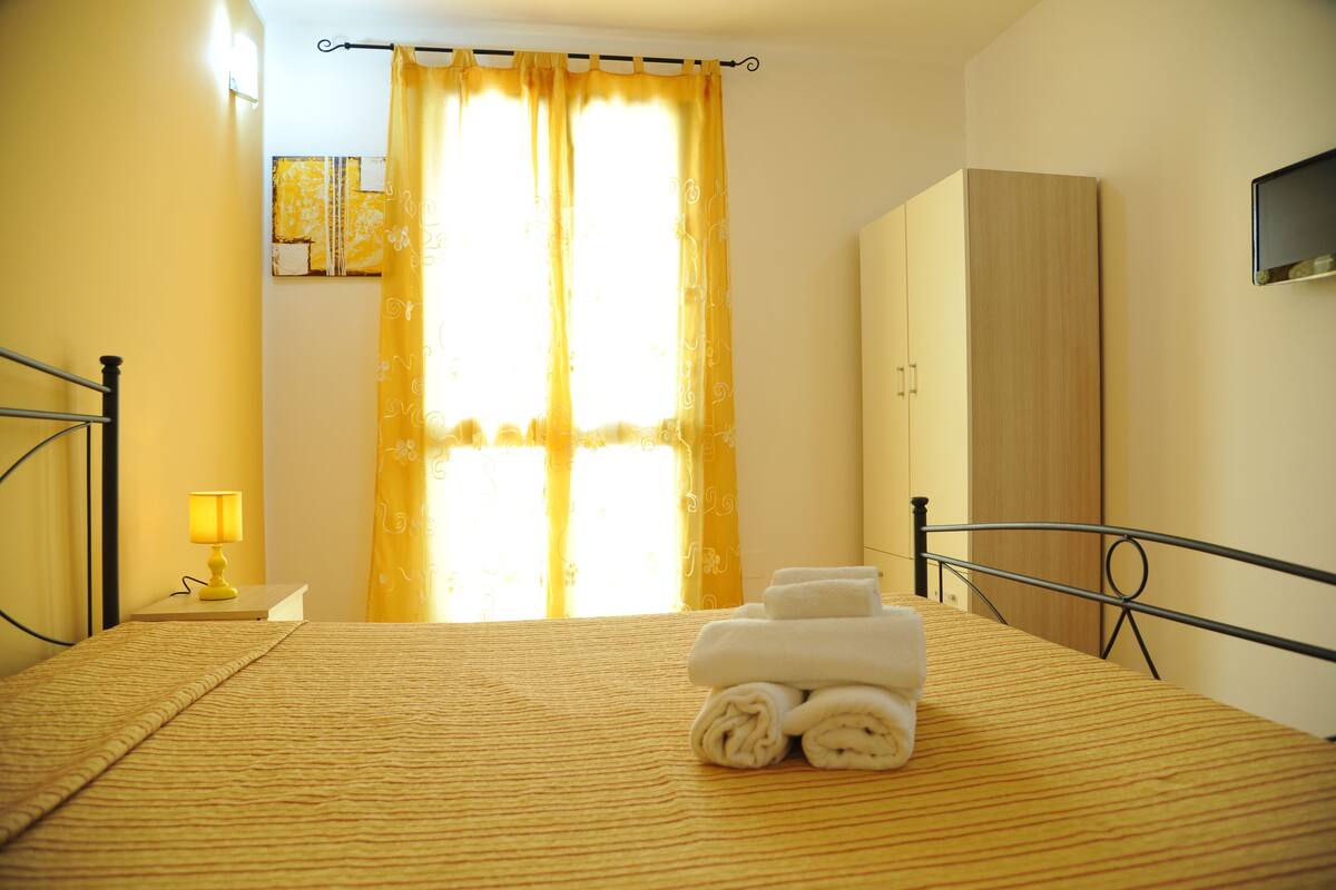 A hotel room with a bed, a bedside lamp, a wardrobe, and a window with curtains.
