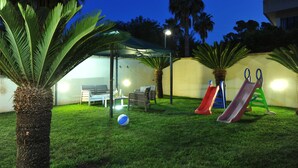 A backyard with artificial grass, a covered seating area, and two children's slides. - B&B Erminia (Presicce-Acquarica)