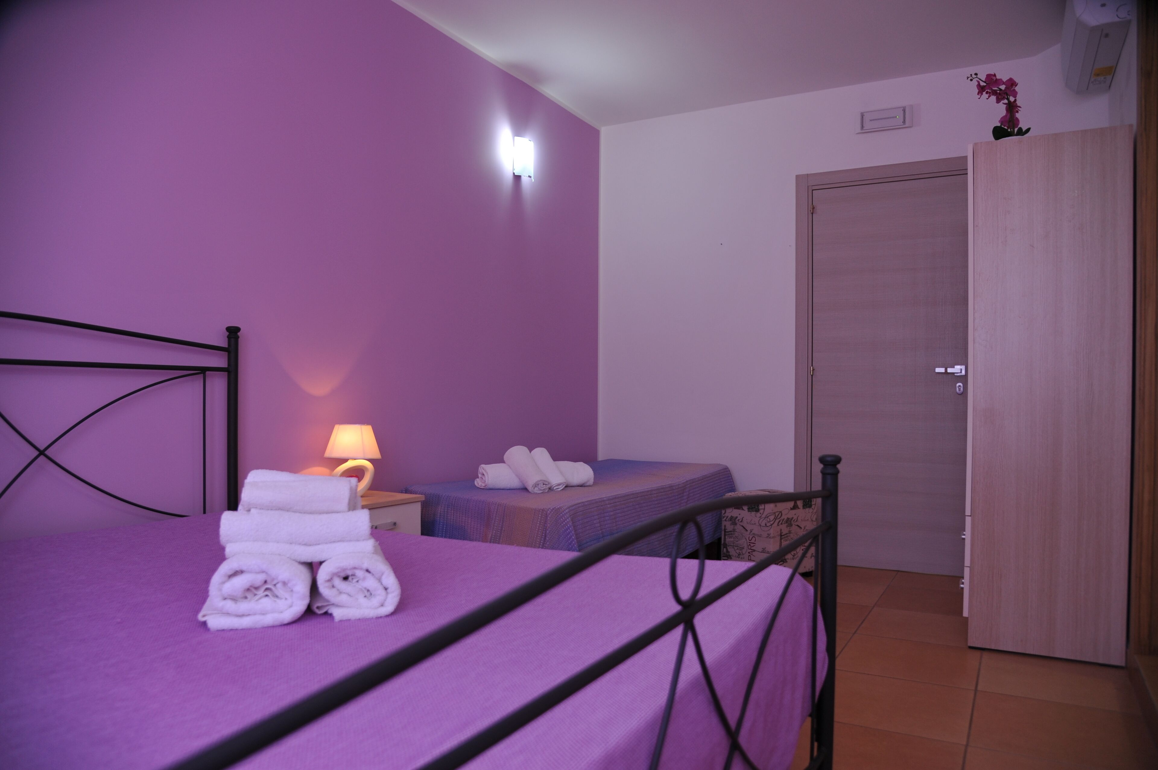 Une chambre à coucher comprenant un lit, une table de chevet avec une lampe, une petite table de chevet avec des serviettes et une armoire.