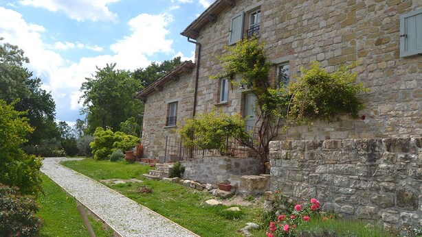 Un edificio de piedra con un camino de grava que conduce a él, rodeado de follaje y flores.