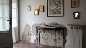 Una habitación con pared de piedra, una mesa de madera con mantel de encaje y cuadros enmarcados en la pared.