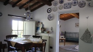 Un comedor con una mesa de madera, sillas y una lámpara colgante. Hay platos decorativos en la pared y un ventanal que proporciona luz natural.