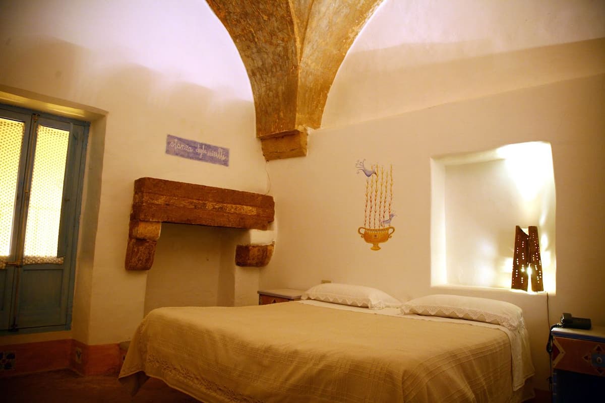A bedroom with a bed, a wooden headboard, a window with curtains, and a wall decoration.