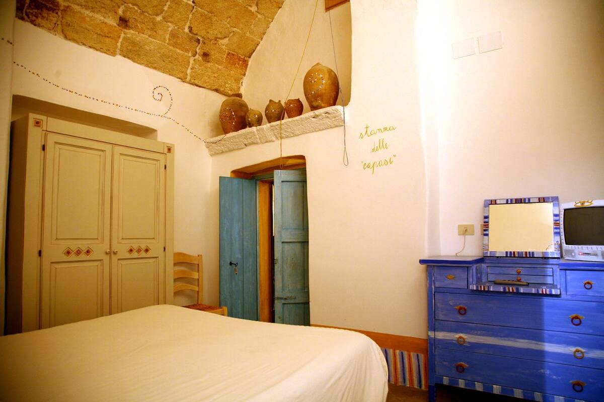 A bedroom with a bed, a dresser, and a shelf with pottery.