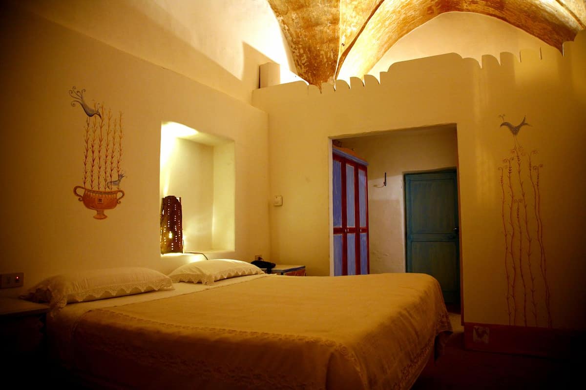 A bedroom with a large bed, a nightstand, a mirror, and a door.