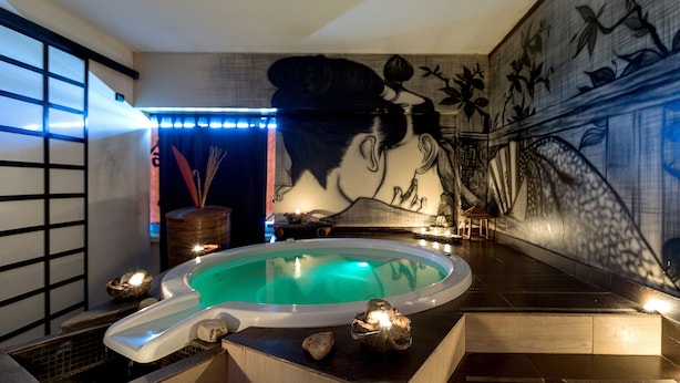 Un área de spa con una bañera de hidromasaje, una pila de piedra y un mural en la pared.