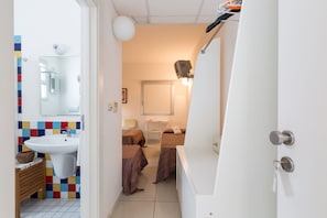 A narrow hotel room with a white sink, a mirror, a bed with a brown bedspread, and a small bedside table. - Silver Hotel (Matino)