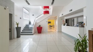 Un moderno vestíbulo de hotel con una escalera, un mostrador de recepción y plantas en macetas.